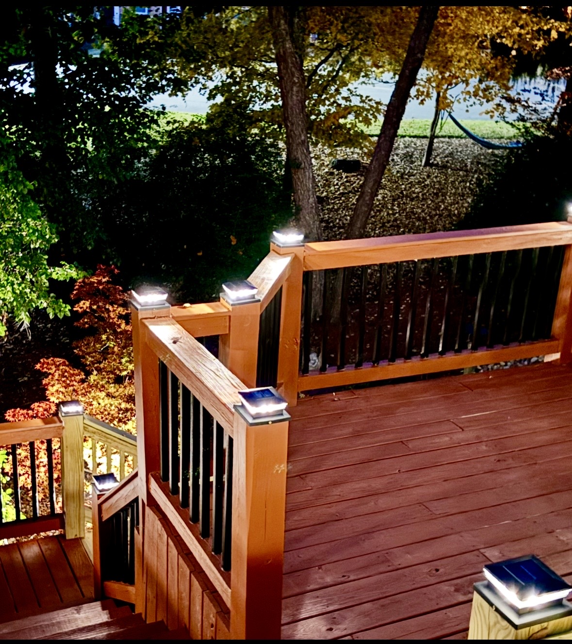 Stained wood deck with black balusters, stairs and illuminated post-cap lights at night