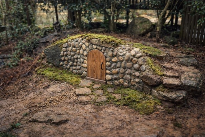 Low rounded stone garden entry with a wooden arched door and moss-covered top